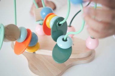 Bir çocuk farklı renkte boncukları tahtaya dizmek için elleri kullanır..