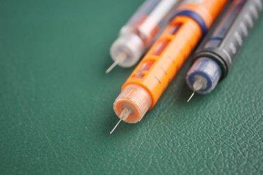 Yeşil bir yüzeyde farklı tipte insülin kalemleri.