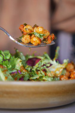 Sıradan bir yemek ortamında nohutlu salata yiyen bir insan..