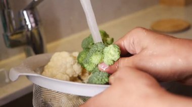 Bir insan akan suyun altında brokoli ve karnabahar yıkar..