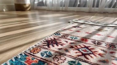 Odaya güneş ışığı girerken ahşap bir zeminde renkli bir halı duruyor..