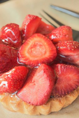 Dilimlenmiş çilekle kaplı bir turta çatalla bir tabakta oturur..