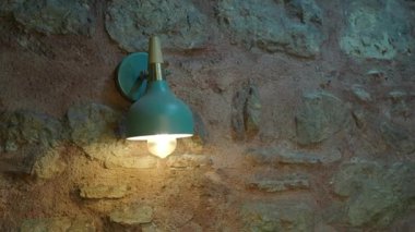 Işıl ışıl yanan bir lamba, kapalı bir alanda taş bir duvarda parlıyor..