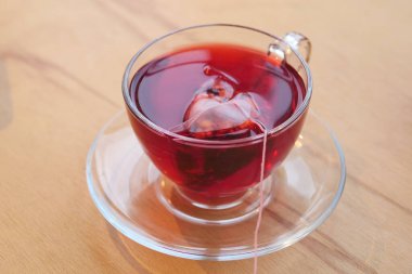 Bir fincan sıcak çay, içinde çay poşeti olan ahşap bir masada oturur..