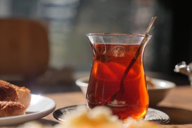 Bir bardak çay, ekmek ve diğer yiyeceklerin yanında bir masada oturur..