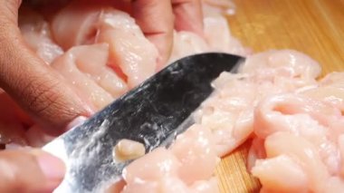 Eller, mutfakta ahşap bir kesme tahtasıyla çiğ tavuk doğruyor..