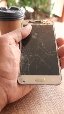 Yanında kahve fincanı olan kırık bir akıllı telefon tutan kişi..