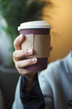 Kafe ortamında koluyla kaplanmış bir bardak tutan kişi..