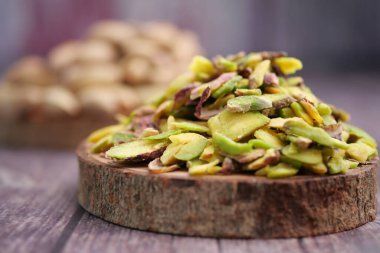 Pistachio nuts are arranged on a wooden board with more in the background.