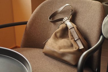 Kahverengi bir çanta sıcak bir yerdeki bir masanın yakınındaki sandalyeye konur..