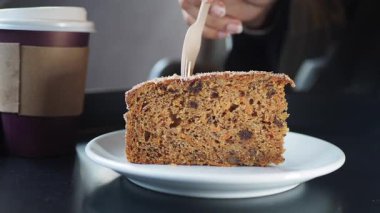 Bir insan elinde kahve tutarken bir dilim pastaya çatal götürür..