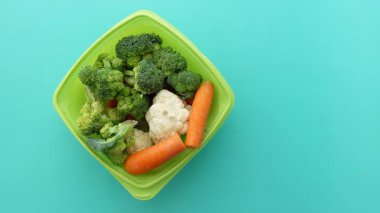 Yeşil ve turuncu sebzelerle dolu bir kase mavi bir masada oturur..