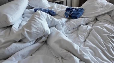 Giysiler dağınık bir yatakta, yumuşak ışıklandırmalı bir odada..