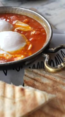 Yumurtalar domates sosunda pişirilir ve masada ekmek servis edilir..