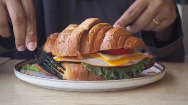 Kişi, kafede taze malzemelerle kruvasan sandviçi hazırlar..