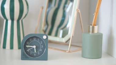 Bir saat dekoratif nesneler ve bir ayna ile çevrili bir rafta durur..