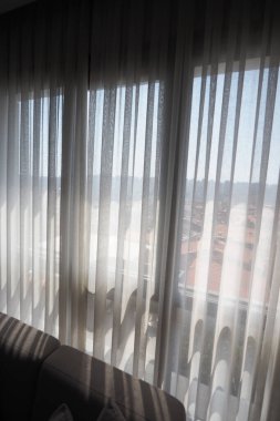 Parlak güneş ışığı bir şehir alanındaki perdelerin arasından parlıyor..