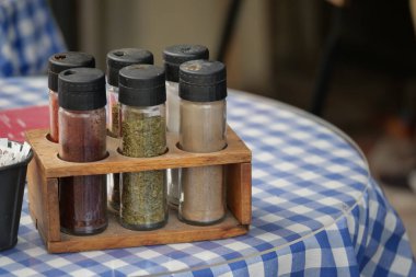 Çeşitli baharat kavanozları kareli bir masada ahşap bir tutacağa oturur..
