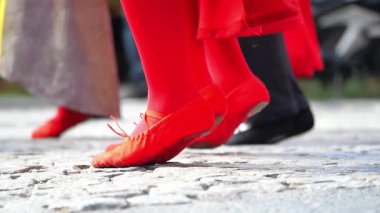 İnsanlar bir etkinlik sırasında taş bir sokakta kırmızı ayakkabılarla dans eder..