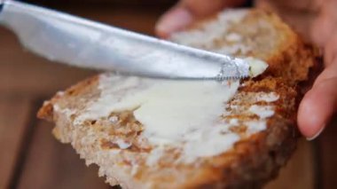 Birisi bir parça ekmek kesiyor ve tereyağı ekliyor..