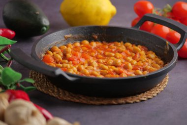 Fasulyeler, masada siyah bir tavada domates ve soğanla pişiriliyor..