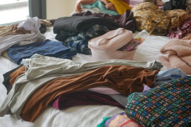 İnsanlar bir odadaki yataklarda giysileri düzenliyor, eşyalar düzenliyorlar..