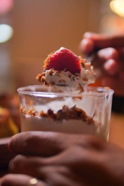 Elinde çırpılmış krema ve fındıklı bir bardak tatlı tutan kişi..