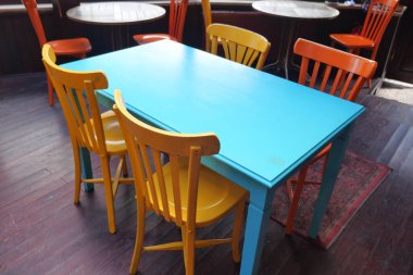 Kafe ortamında mavi bir masanın etrafına renkli sandalyeler dizilir..