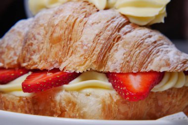 Kruvasan üzerinde krema ve taze çilek olan bir tabakta oturur..