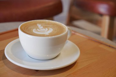 Beyaz fincanda sıcak kahve ve ahşap bir yüzey üzerinde latte sanatı.