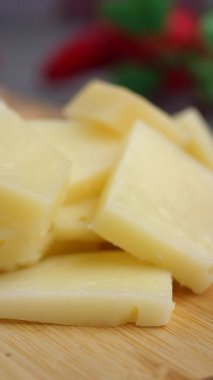 Slices of cheese are arranged on a wooden board with herbs nearby.