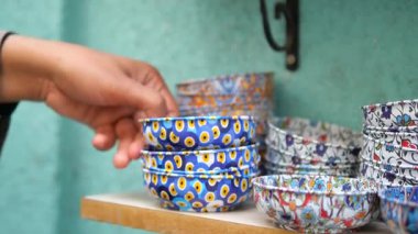 Person selects decorative bowls from shelf in market space.