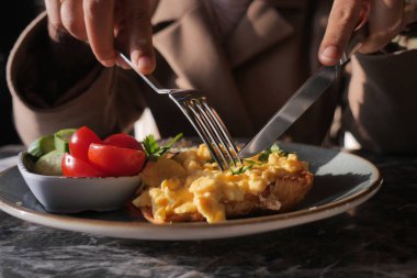 Bir insan, yanında domates ve salatalık olan bir tabak yumurtayı keser..