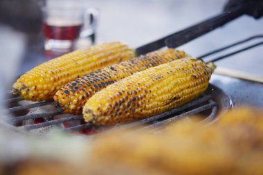 Üç mısır tanesi ızgarada pişiyor ve duman yükseliyor..