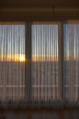 Gün doğumu, sessiz renklerle dolu bir odada, perdelerin arkasında belirir..