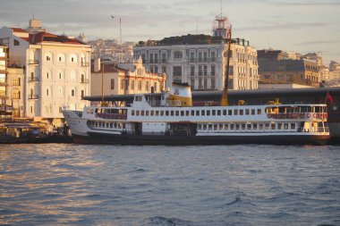 Gün batımında arka planda şehir binaları olan bir limana bir feribot yanaşıyor..