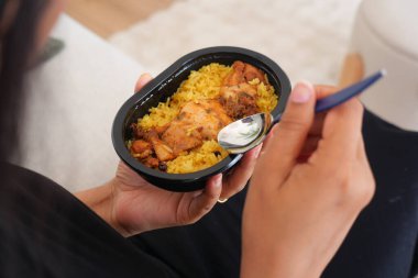 Birisi kaşık ile plastik bir kabın içinden tavuk ve pirinç yiyor..