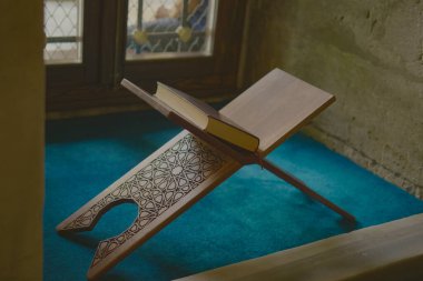 Ahşap tezgah caminin penceresinin yanında açık bir Kur 'an tutuyor. .