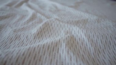 Kamera, küçük çizgileri olan beyaz bir yatak çarşafının detaylarını gösteriyor..