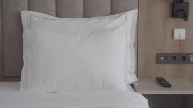 Bir otel yatağında, komodinin yanındaki yastığa yakından bak..