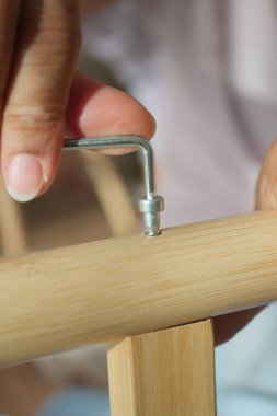 A person uses a tool to attach a part to wooden furniture during assembly.