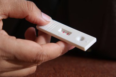 Bir el, iki görünür çizgi gösteren hamilelik testi setini tutuyor. .