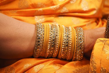 Parlak bileziklerle süslenmiş bir bilek parlak turuncu kumaşa dayanır..