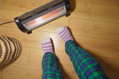 Kişi, ahşap zeminde taşınabilir ısıtıcının yanında sıcak çoraplar içinde durur..