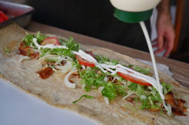 Bir insan, salata ve domates gibi malzemeler ekleyerek büyük bir paket hazırlar..