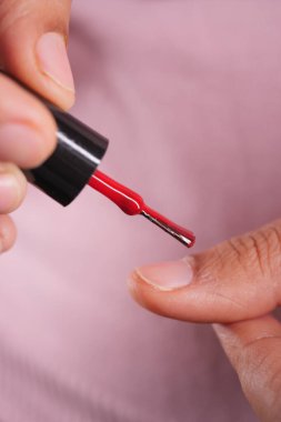 Bir insan kırmızı tırnak cilasını parmağının üstünde tutar..