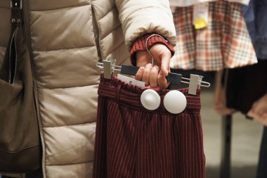 Dükkanda düğmeleri olan kırmızı bir etek tutan biri var..