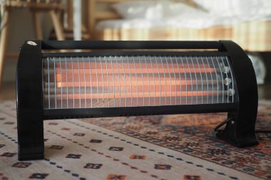 Yumuşak ışıklandırmalı ve mobilyalı bir odada halının üzerinde bir ısıtıcı duruyor..