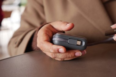 Kafedeki bir masada oturan biri, elinde tek eliyle küçük bir cihaz tutuyor..