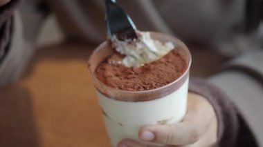 Bir insan elinde katmanlı ve malzemeli bir fincan tatlı tutuyor..